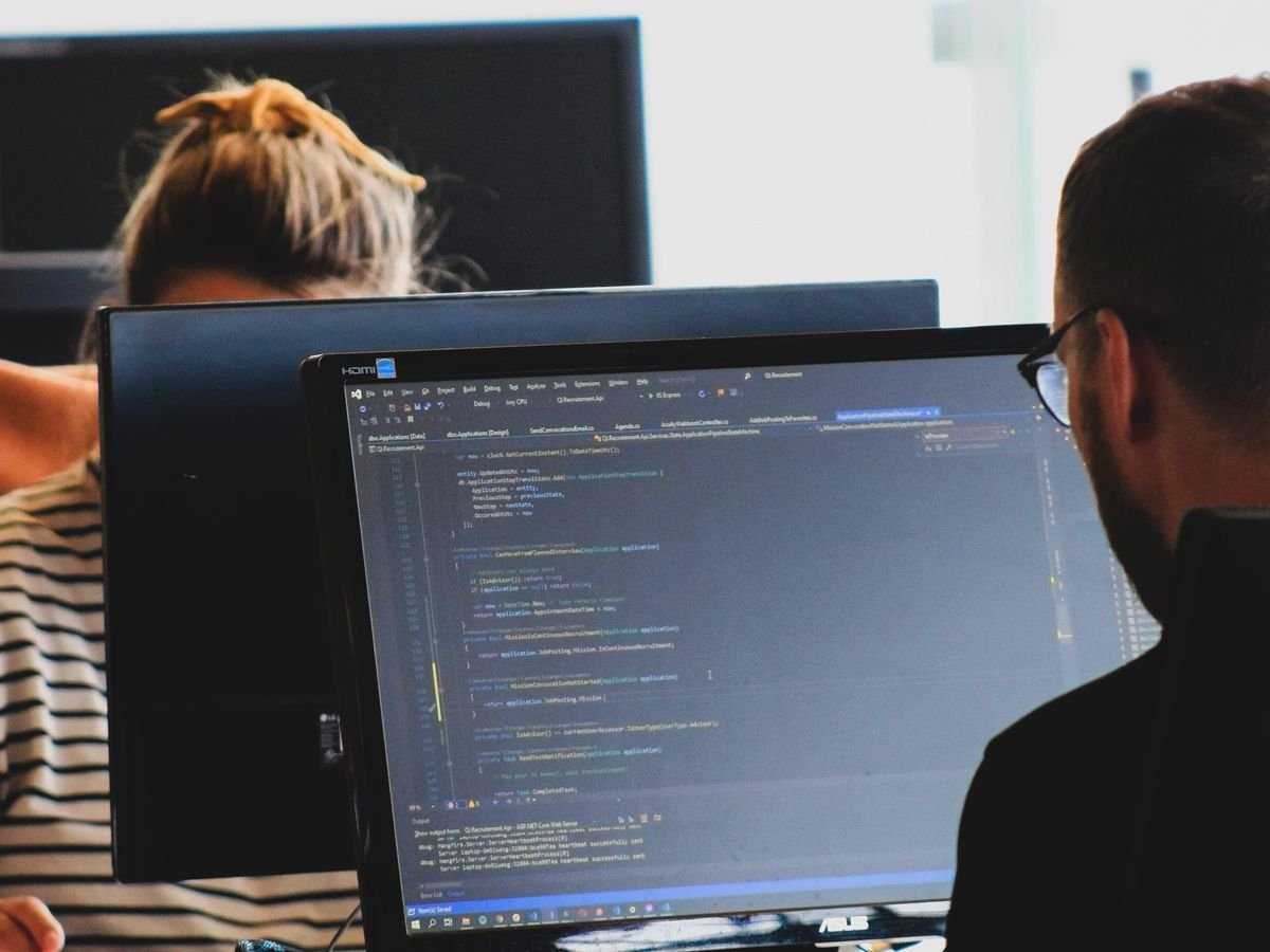 Two people sit at monitors coding