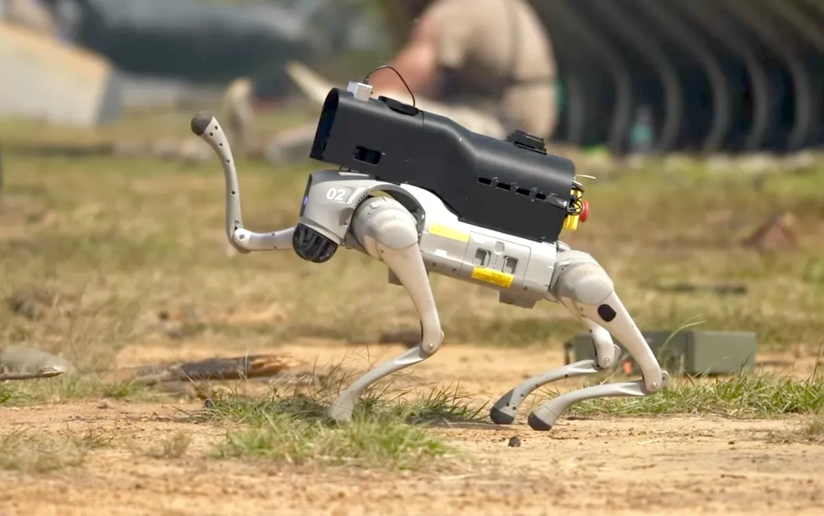 Four-legged robot with camera moving across grassy terrain.