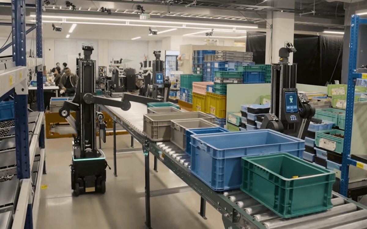 Robotic arms on mobile bases sort crates on a conveyor belt in a warehouse