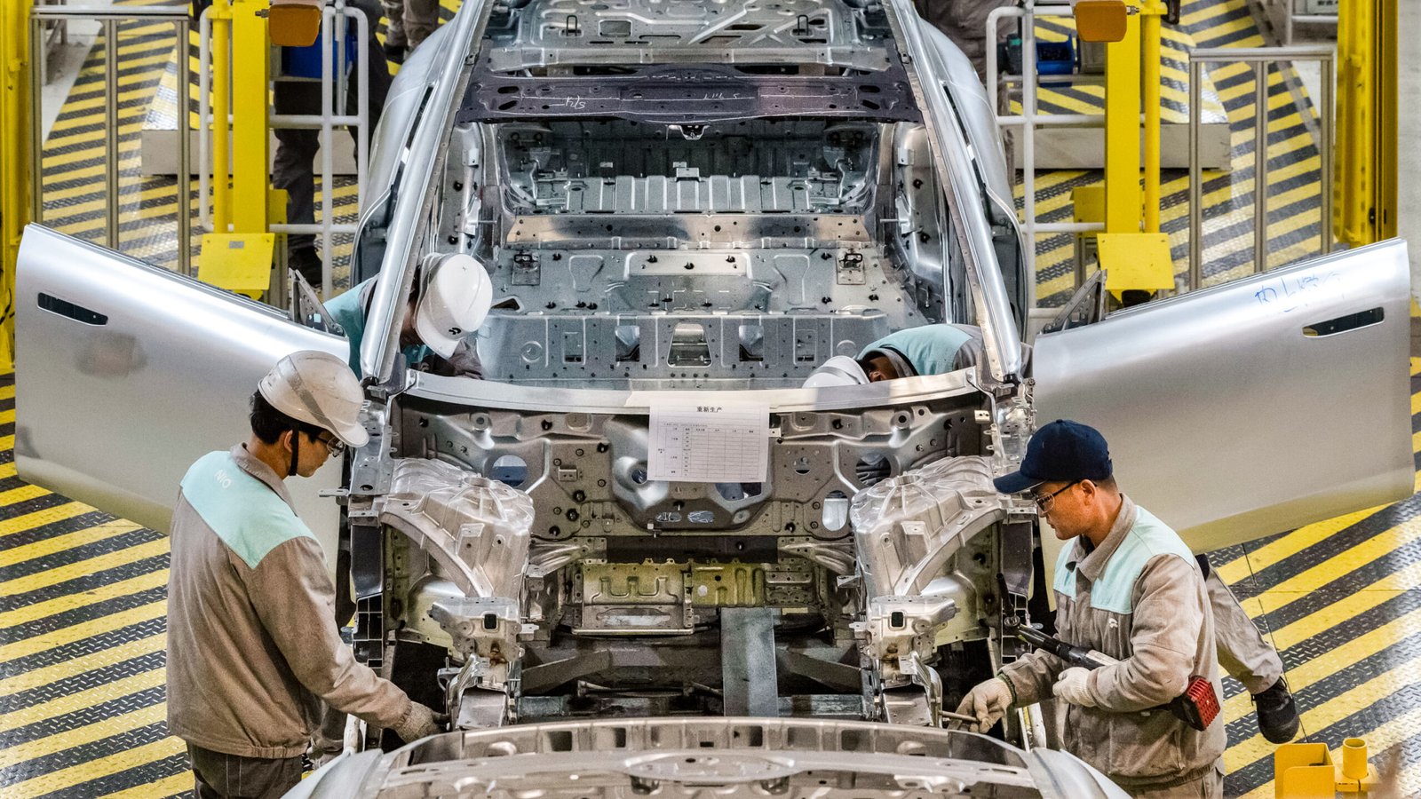 Workers from Chinese electric vehicle (EV) company NIO inspect a vehicle chassis on an automated production line