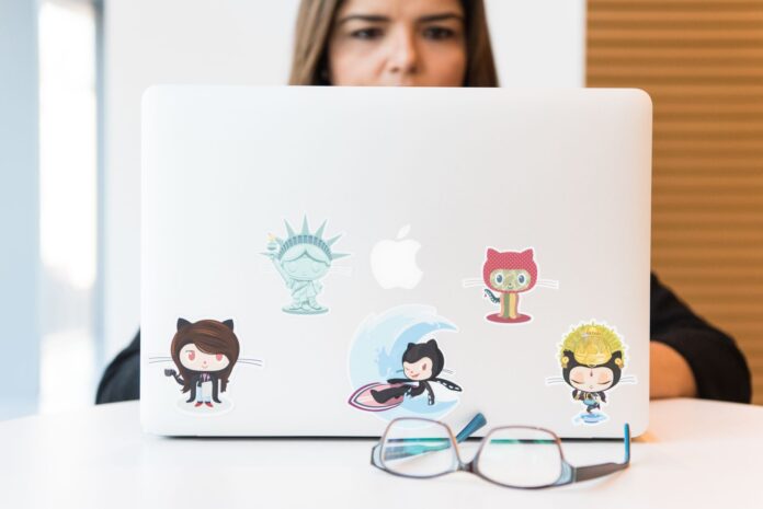 Woman focused on laptop with colorful GitHub-themed stickers, eyeglasses in foreground
